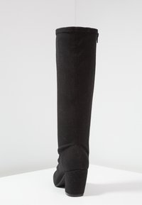 Bota negra de sobre la rodilla, hecha de un tejido elástico con tacón ancho, que presenta una textura suave y una cremallera trasera para el cierre.