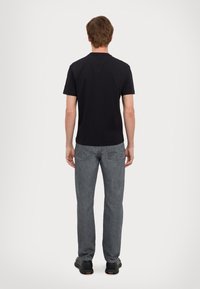 T-shirt nera a maniche corte con vestibilità classica, abbinata a jeans grigi e sneakers nere, vista da dietro su uno sfondo semplice.