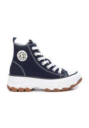 Zapatilla de caña alta azul marino con cordones blancos, suela blanca gruesa, banda de rodadura marrón y parche redondo con logo en el lateral.