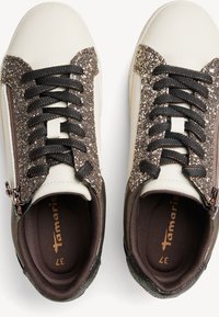 Zapatillas blancas y marrones con un upper brillante marrón, cordones negros y cremallera lateral, que cuentan con un suave forro interior y detalles cosidos.