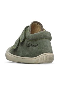 Chaussure en daim vert avec une sangle Velcro, semelle en caoutchouc beige et coutures jaunes contrastées. Présente une forme arrondie et une texture douce.