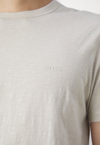 T-shirt beige clair à manches courtes, fabriqué en tissu doux, comportant un petit logo en relief "BOSS" sur la partie gauche de la poitrine.