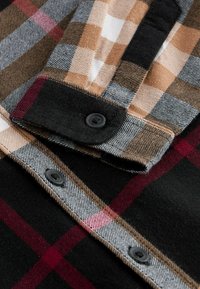 Flanellskjorta med ett svart, brunt och vinrött rutmönster, med en mjuk textur, en knappad krage och svarta knappar.