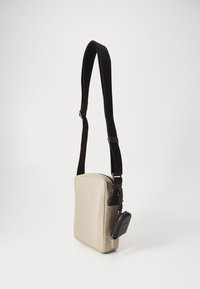 Borsa a tracolla beige con superficie liscia, tracolla nera regolabile, forma rettangolare e una pochette nera con zip removibile attaccata.