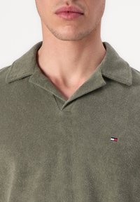 Zelená polo košeľa z jemnej tkaniny s golierom a malým vyšívaným logom na ľavej hrudi. Má klasický strih a štruktúrovaný povrch.