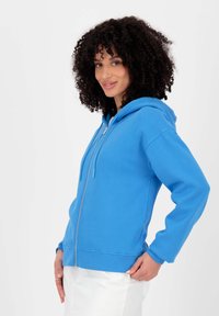 Blauwe rits-hoodie van katoen, met een capuchon, lange mouwen en ribgebreide manchetten. De stof lijkt zacht met een gladde textuur.