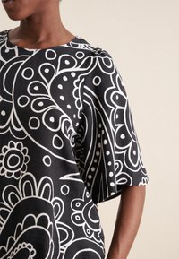 Maglietta nera con design paisley e floreale bianco. Maniche corte, scollatura rotonda e texture del tessuto morbida. Motivi dettagliati su tutta la superficie.