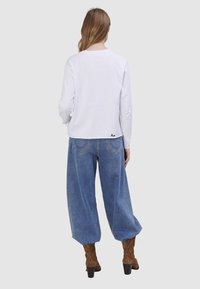 Weißes Langarmhemd kombiniert mit hoch taillierter, locker sitzender blauer Jeans aus Denim, mit geschwungenem Saum und dezentem Rückennähdetail.