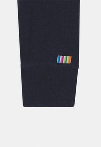 Le bas de jambe en tricot bleu marine présente une étiquette rayée multicolore avec des rayures rouges, orange, jaunes, vertes, bleues et violettes sur le côté.