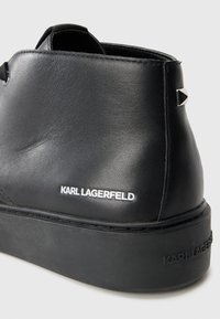 Zapatilla alta de cuero negra con acabado texturizado, suela de plataforma, detalles de logo y acentos en triángulo plateado.