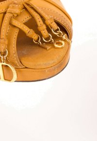 Sandale en cuir marron avec des brides croisées et des charms dorés en forme de lettres formant le mot « Dior » attachés aux brides avant.