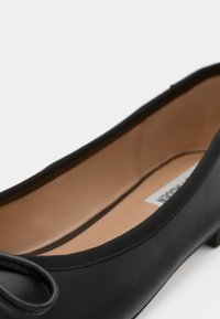 Mustad musta ballettijalatsid sileda nahast üle osa, ümar varvas, väike paela detail ja beež interjöör. Madal konts, minimalistlik disain.