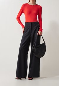 Haut rouge à manches longues associé à un pantalon large noir taille haute. Accessoirisé avec un sac à main noir rond présentant des coutures arrondies.