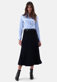 Helles blaues Satinhemd mit Knöpfen, kombiniert mit einem dunklen, plissierten Rock und schwarzen Stiefeletten. Glatte Textur und taillierte Passform.