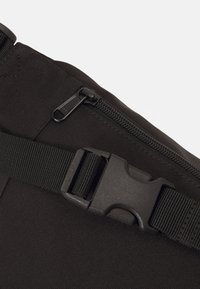 Borsa a tracolla nera con cerniera, tracolla regolabile e fibbia in plastica. Realizzata in tessuto resistente con superficie testurizzata.