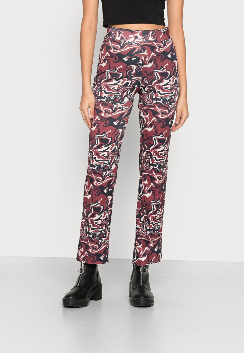 Calças ajustadas de cintura alta com um padrão abstrato em vermelho, preto e creme. Tecido suave, design de perna larga, combinadas com botas de tornozelo pretas.