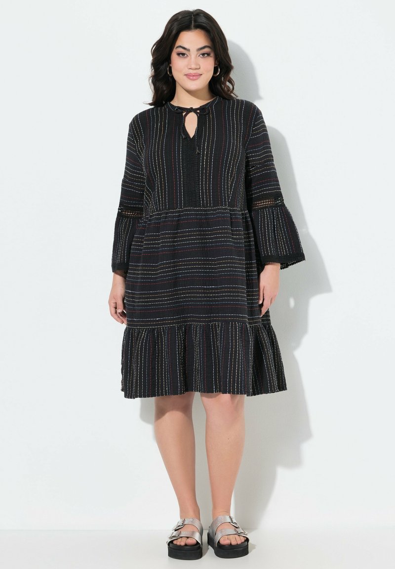 Robe noire avec des rayures horizontales multicolores, des manches évasées, un décolleté en trou de serrure et un ourlet à volants en couches. Le matériau semble texturé.