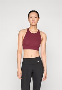 Bordo sportski grudnjak s dizajnom racerback, glatke teksture i detaljem logotipa. Uparen s crnim tajicama visokog struka s suptilnim naglascima.