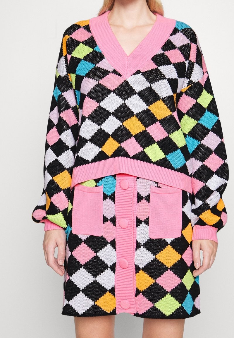 Zwart, roze, wit en kleurrijk ruitbreisel gebreide jurk met een V-hals, oversized mouwen en roze knoopaccenten. Beschikt over twee voorzakken.