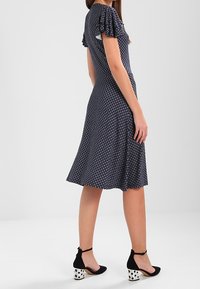 Námořnické modré šaty s květinovým vzorem, krátké ruflové rukávy, rozšířený lem. V kombinaci s černými botami na blokovém podpatku s puntíky.