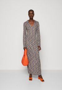 Maxi abito in tessuto testurizzato con un motivo multicolore; presenta maniche lunghe e scollatura a V profonda. Accompagnato da una borsa arancione e scarpe.