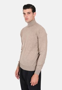 Maglione a collo alto beige realizzato in morbido tessuto lavorato a maglia. Design aderente con maniche lunghe e colletto a coste, abbinato a pantaloni scuri.