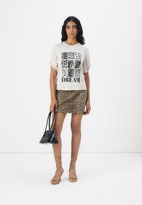 T-shirt blanc avec motif animal noir en grille et texte "DREAM", associé à une mini-jupe à imprimé léopard et un sac à main noir. Sandales à lanières beige.