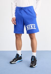 Niebieskie spodenki wykonane z mieszanki bawełny, z elastycznym pasem ze sznurkiem i białym logo "NIKE" na lewym udzie. Czarne sneakersy z niebieskimi akcentami.