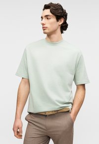 Ανοιχτό πράσινο κοντομάνικο μπλουζάκι με στρογγυλή λαιμόκοψη, κατασκευασμένο από μαλακό ύφασμα, σε συνδυασμό με καφέ παντελόνι με υφή και μπεζ ζώνη.