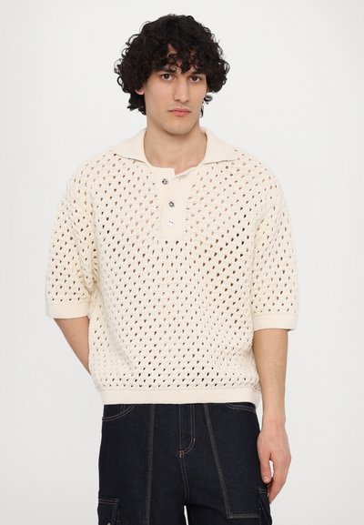 Pull polo en tricot crème avec un motif ajouré, manches courtes et un col avec trois boutons et des poignets côtelés.