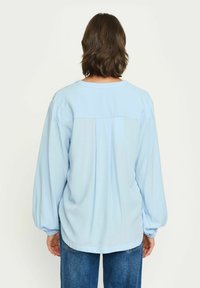 Camicia azzurra chiara a maniche lunghe con vestibilità comoda, caratterizzata da un design con yoke e maniche arricciate. Tessuto morbido, orlo arrotondato e stile casual.