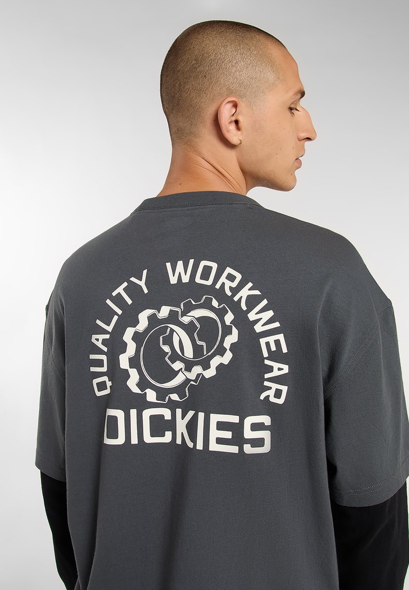 Gray short-sleeve t-shirt featuring a large white graphic of gears and text "QUALITY WORKWEAR DICKIES" on the back. Soft cotton material.