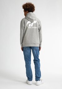 Felpa grigia con grande logo bianco "Gran Turismo" sul retro. Abbinata a jeans blu e sneakers bianche. Tessuto morbido, vestibilità rilassata.