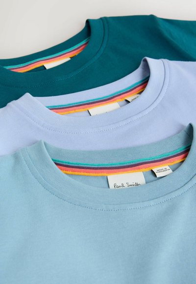 Tres camisetas con cuello redondo apiladas: azul verdoso oscuro, azul claro y azul pastel. Cada una tiene un ribete en el cuello con rayas multicolores.
