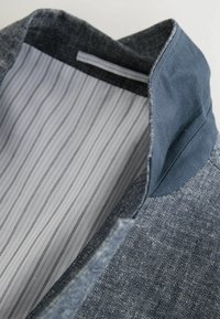 Interiorul unei jachete din denim cu o căptușeală în dungi gri deschis și alb, guler albastru închis în contrast și un material exterior texturat.