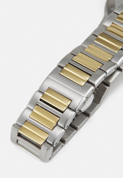 Stainless steel watch bracelet with alternating gold accents, featuring a smooth texture and square link design, engraved with "Ferragamo."