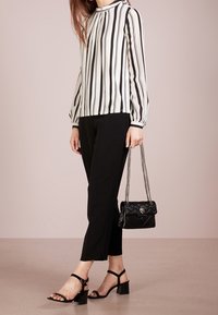 Svartvit randig blus med långa ärmar, svarta korta byxor, svarta klackskor med remmar och en quiltad svart handväska med kedjerem.