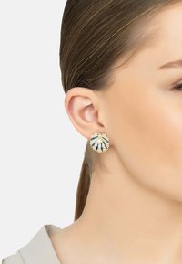 Pendientes en tono dorado con forma de concha, que cuentan con un centro de perla blanca, acentos de esmalte azul y detalles de piedras preciosas claras.