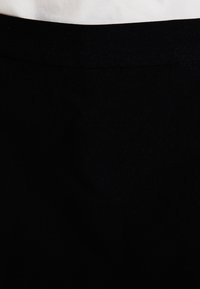 Černá tkanina s měkkou strukturou, která má hladký pas. Design je minimalistický a vystihuje jednobarevnost bez vzorů.