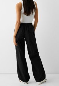 Svarta, lätta, löst sittande byxor med elastisk midja, två bakfickor och en slät textur, kombinerat med en tajt vit linne.