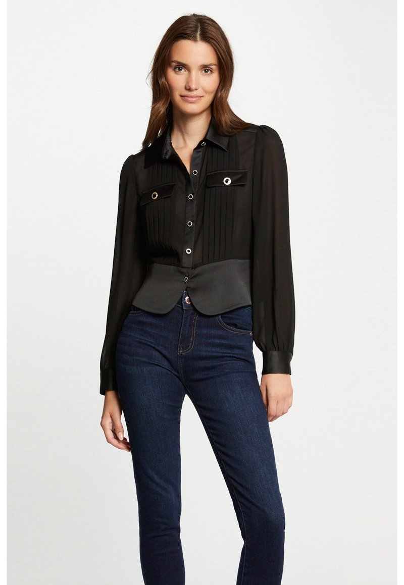 Blusa negra plisada con mangas largas, cierre de botones y bolsillos en el pecho abiertos; presenta una cintura entallada y una textura suave.