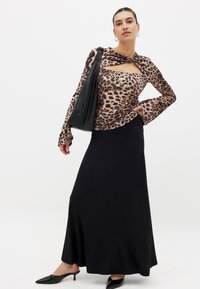 Leopard print long-sleeve top with a cut-out design, paired with a black fitted maxi skirt. A black shoulder bag and black pointed heels complete the look.
