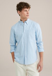 Lichtblauw overhemd met knopen, gemaakt van gestructureerde stof, met een borstzak en opgerolde mouwen, gecombineerd met crèmekleurige broek.