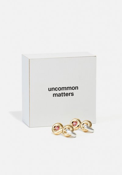 Orecchini d'oro e argento con gemme rosa in un design ritorto, confezionati in una scatola bianca etichettata "uncommon matters."