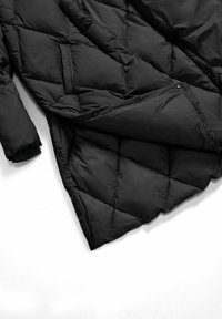 Giacca nera imbottita con design trapuntato, dotata di tasca e chiusure a scatto sul davanti. Il materiale appare leggero e liscio.