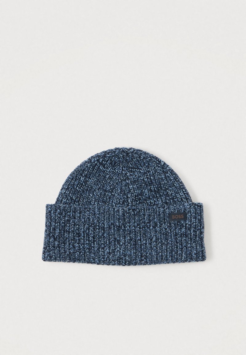 Tumši zila adīta cepure ar salocītu apmali. Izgatavota no mīksta materiāla ar teksturētu virsmu un mazu logotipa uzšuvumu.