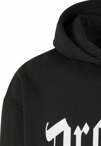 Svart hettegenser med myk tekstur, med bold hvite bokstavgrafikker på forsiden og et avslappet passformdesign.