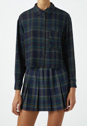 Marineblaue karierten Cropped-Bluse mit gelben und grünen Akzenten, Wurst und Brusttasche, kombiniert mit einem passenden gefältelten Rock.