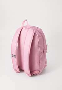 Roze rugzak van gevoerd stof, voorzien van twee schouderbanden, een handvat aan de bovenkant en een ritszak aan de zijkant. Eenvoudig, rond ontwerp.