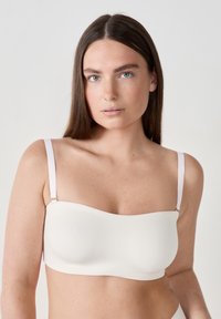 Reggiseno strapless color beige chiaro con una texture liscia, coppe sagomate e spalline regolabili di un tenue colore chiaro con dettagli in metallo dorato.